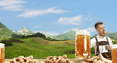 Image showing The happy smiling man with beer dressed in traditional Austrian or Bavarian costume holding mug of beer, mountains on background, flyer
