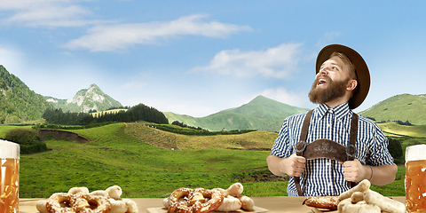Image showing The happy smiling man with beer dressed in traditional Austrian or Bavarian costume holding mug of beer, mountains on background, flyer