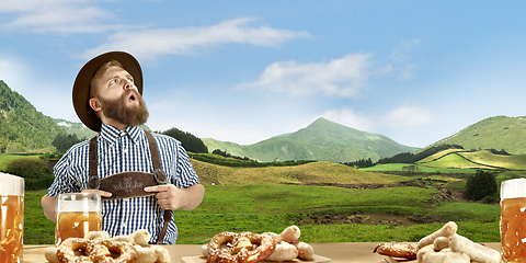 Image showing The happy smiling man with beer dressed in traditional Austrian or Bavarian costume holding mug of beer, mountains on background, flyer