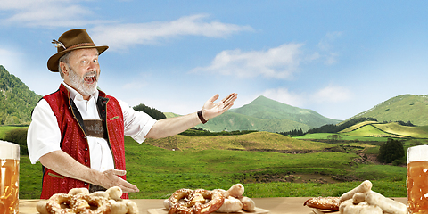 Image showing The senior happy smiling man with beer dressed in traditional Austrian or Bavarian costume holding mug of beer, mountains on background, flyer