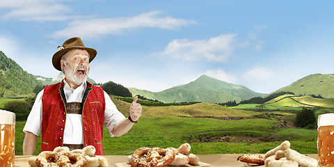 Image showing The senior happy smiling man with beer dressed in traditional Austrian or Bavarian costume holding mug of beer, mountains on background, flyer