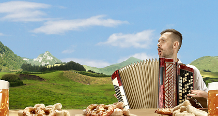 Image showing The happy smiling man with beer dressed in traditional Austrian or Bavarian costume holding mug of beer, mountains on background, flyer