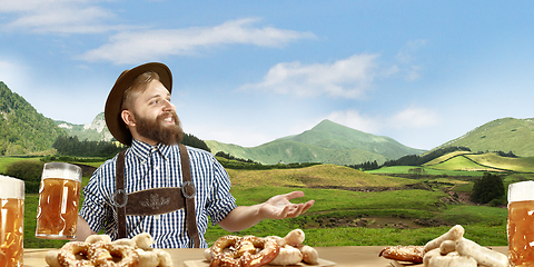 Image showing The happy smiling man with beer dressed in traditional Austrian or Bavarian costume holding mug of beer, mountains on background, flyer