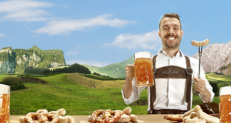 Image showing The happy smiling man with beer dressed in traditional Austrian or Bavarian costume holding mug of beer, mountains on background, flyer