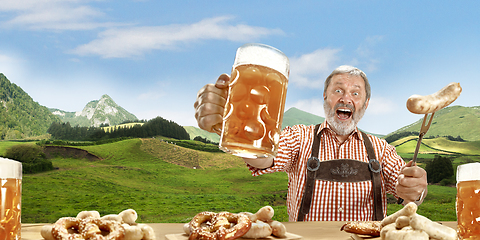 Image showing The senior happy smiling man with beer dressed in traditional Austrian or Bavarian costume holding mug of beer, mountains on background, flyer