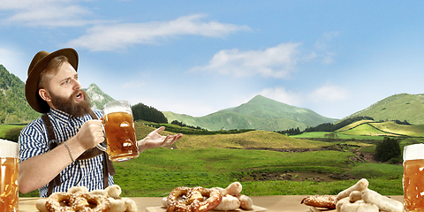 Image showing The happy smiling man with beer dressed in traditional Austrian or Bavarian costume holding mug of beer, mountains on background, flyer