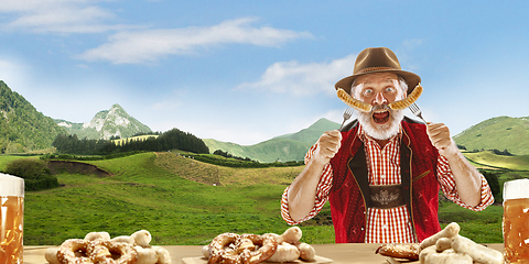 Image showing The senior happy smiling man with beer dressed in traditional Austrian or Bavarian costume holding mug of beer, mountains on background, flyer