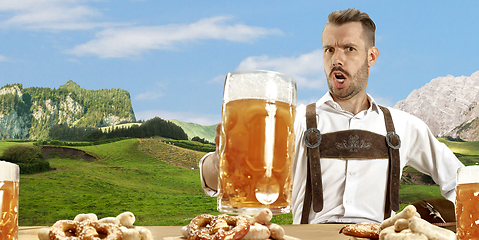 Image showing The happy smiling man with beer dressed in traditional Austrian or Bavarian costume holding mug of beer, mountains on background, flyer