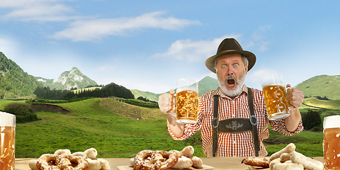 Image showing The senior happy smiling man with beer dressed in traditional Austrian or Bavarian costume holding mug of beer, mountains on background, flyer