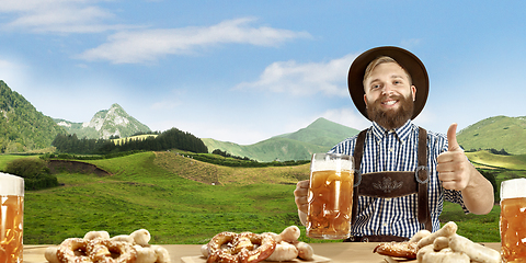 Image showing The happy smiling man with beer dressed in traditional Austrian or Bavarian costume holding mug of beer, mountains on background, flyer