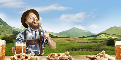 Image showing The happy smiling man with beer dressed in traditional Austrian or Bavarian costume holding mug of beer, mountains on background, flyer