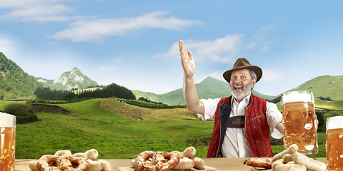 Image showing The senior happy smiling man with beer dressed in traditional Austrian or Bavarian costume holding mug of beer, mountains on background, flyer