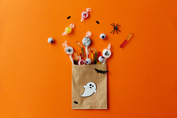 Image showing halloween sweets in paper bag on orange background