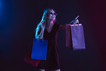 Image showing Portrait of young woman in neon light on dark backgound. The human emotions, black friday, cyber monday, purchases, sales, finance concept.