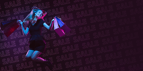 Image showing Portrait of young woman in neon light on dark backgound. The human emotions, black friday, cyber monday, purchases, sales, finance concept. Neoned lettering.