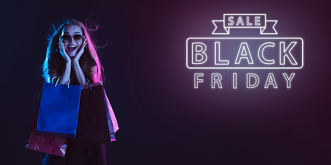 Image showing Portrait of young woman in neon light on dark backgound. The human emotions, black friday, cyber monday, purchases, sales, finance concept. Neoned lettering.