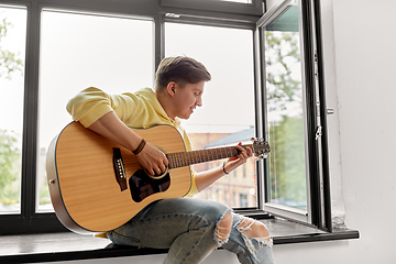 Image showing young man playing guitar sitting on windowsill