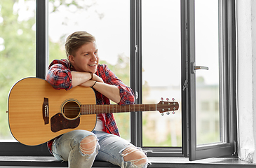 Image showing young man playing guitar sitting on windowsill