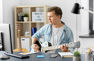 Image showing young man with computer playing guitar at home