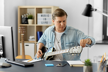 Image showing young man with computer playing guitar at home