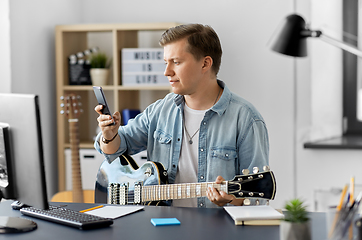 Image showing young man with smartphone and guitar at home