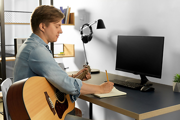 Image showing man with guitar writing to music book at home