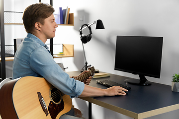 Image showing young man with computer playing guitar at home