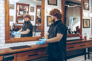 Image showing Male barber at the barbershop wearing gloves preparing working place for client