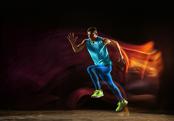 Image showing Professional male runner training isolated on black studio background in mixed light