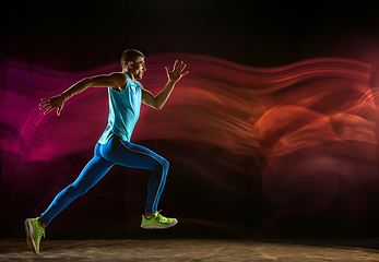 Image showing Professional male runner training isolated on black studio background in mixed light