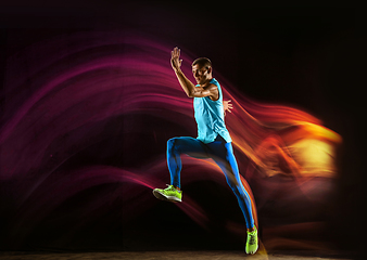 Image showing Professional male runner training isolated on black studio background in mixed light