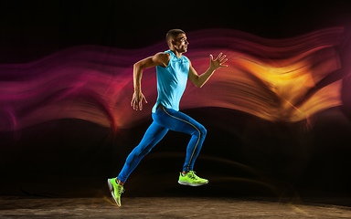 Image showing Professional male runner training isolated on black studio background in mixed light