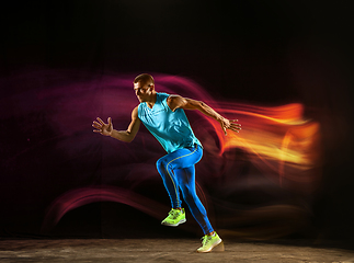 Image showing Professional male runner training isolated on black studio background in mixed light