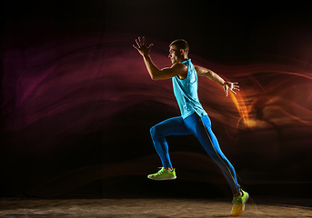 Image showing Professional male runner training isolated on black studio background in mixed light