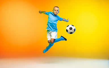 Image showing Young boy as a soccer or football player in sportwear practicing on gradient yellow studio background in neon light