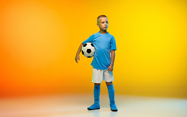 Image showing Young boy as a soccer or football player in sportwear practicing on gradient yellow studio background in neon light