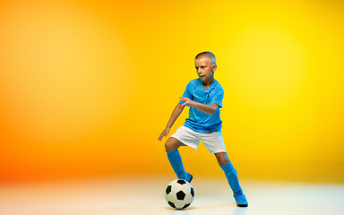 Image showing Young boy as a soccer or football player in sportwear practicing on gradient yellow studio background in neon light