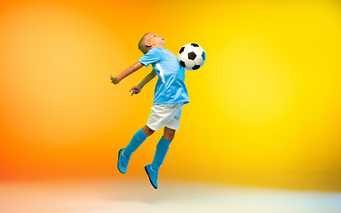 Image showing Young boy as a soccer or football player in sportwear practicing on gradient yellow studio background in neon light