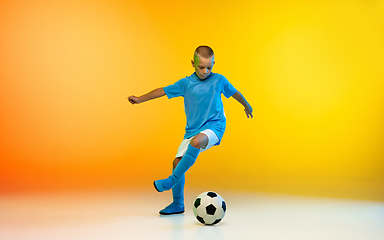 Image showing Young boy as a soccer or football player in sportwear practicing on gradient yellow studio background in neon light