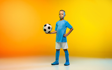 Image showing Young boy as a soccer or football player in sportwear practicing on gradient yellow studio background in neon light