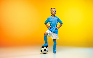 Image showing Young boy as a soccer or football player in sportwear practicing on gradient yellow studio background in neon light