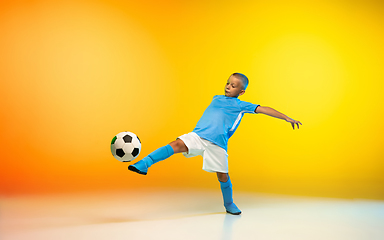 Image showing Young boy as a soccer or football player in sportwear practicing on gradient yellow studio background in neon light