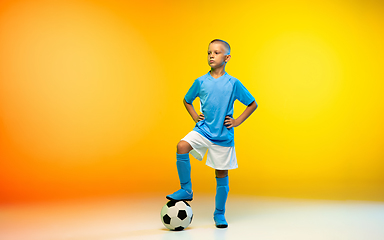 Image showing Young boy as a soccer or football player in sportwear practicing on gradient yellow studio background in neon light