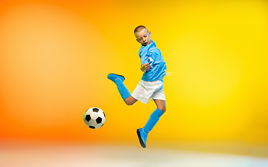 Image showing Young boy as a soccer or football player in sportwear practicing on gradient yellow studio background in neon light