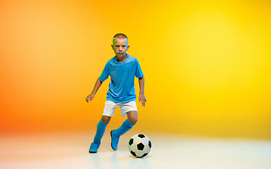 Image showing Young boy as a soccer or football player in sportwear practicing on gradient yellow studio background in neon light