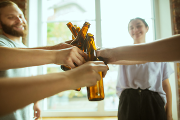 Image showing Young group of friends drinking beer, having fun, laughting and celebrating together. Close up clinking beer bottles