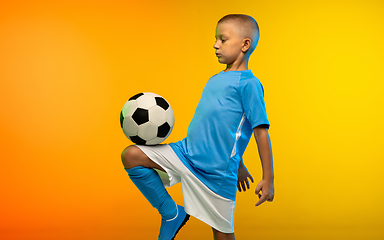 Image showing Young boy as a soccer or football player in sportwear practicing on gradient yellow studio background in neon light