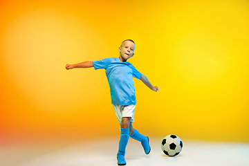 Image showing Young boy as a soccer or football player in sportwear practicing on gradient yellow studio background in neon light