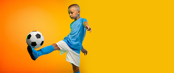 Image showing Young boy as a soccer or football player in sportwear practicing on gradient yellow studio background in neon light