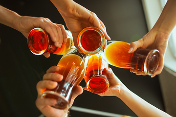 Image showing Young group of friends drinking beer, having fun, laughting and celebrating together. Close up clinking beer glasses